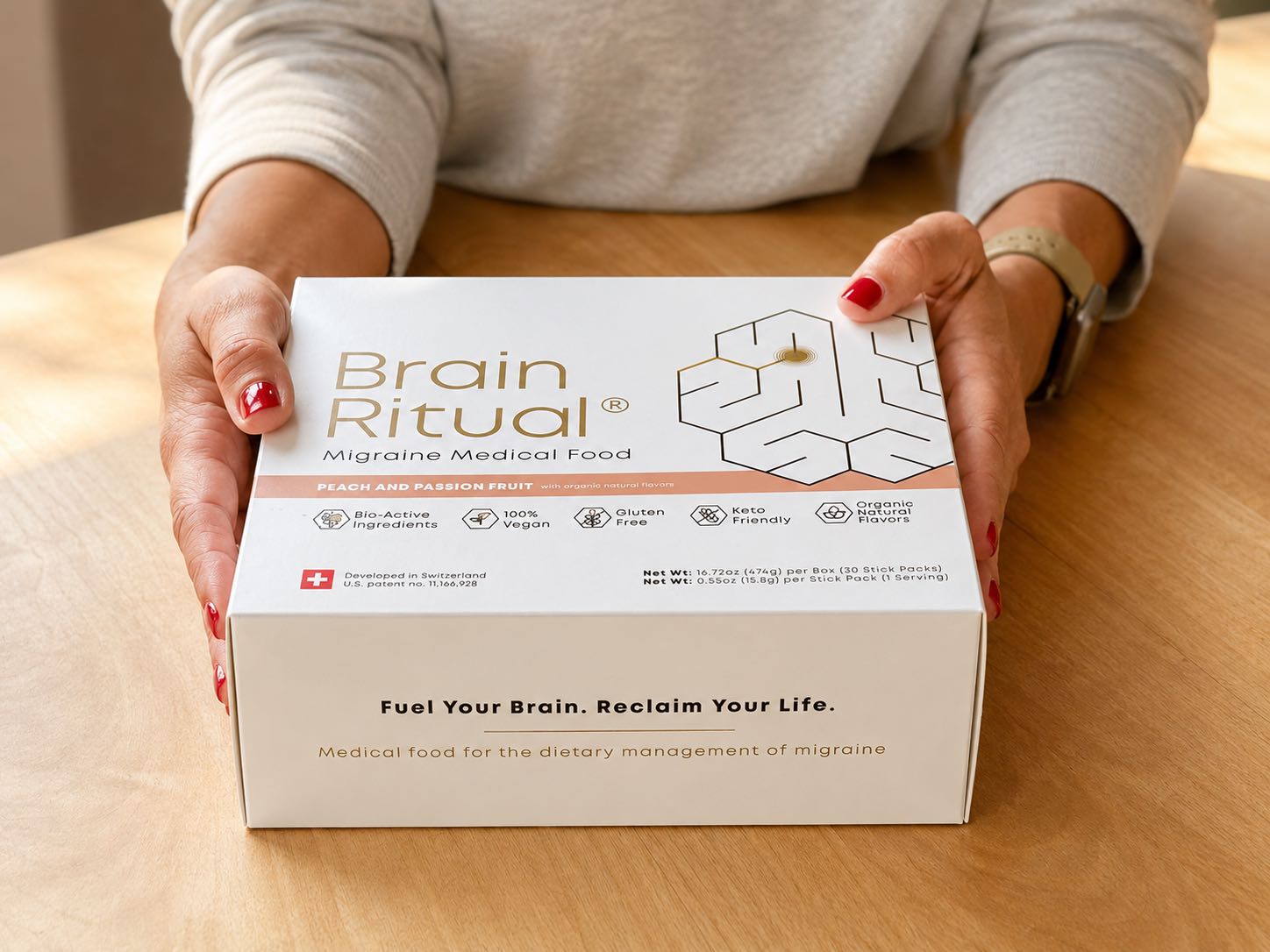 Two hands resting on a Brain Ritual Migraine Medical Food box on a wooden table