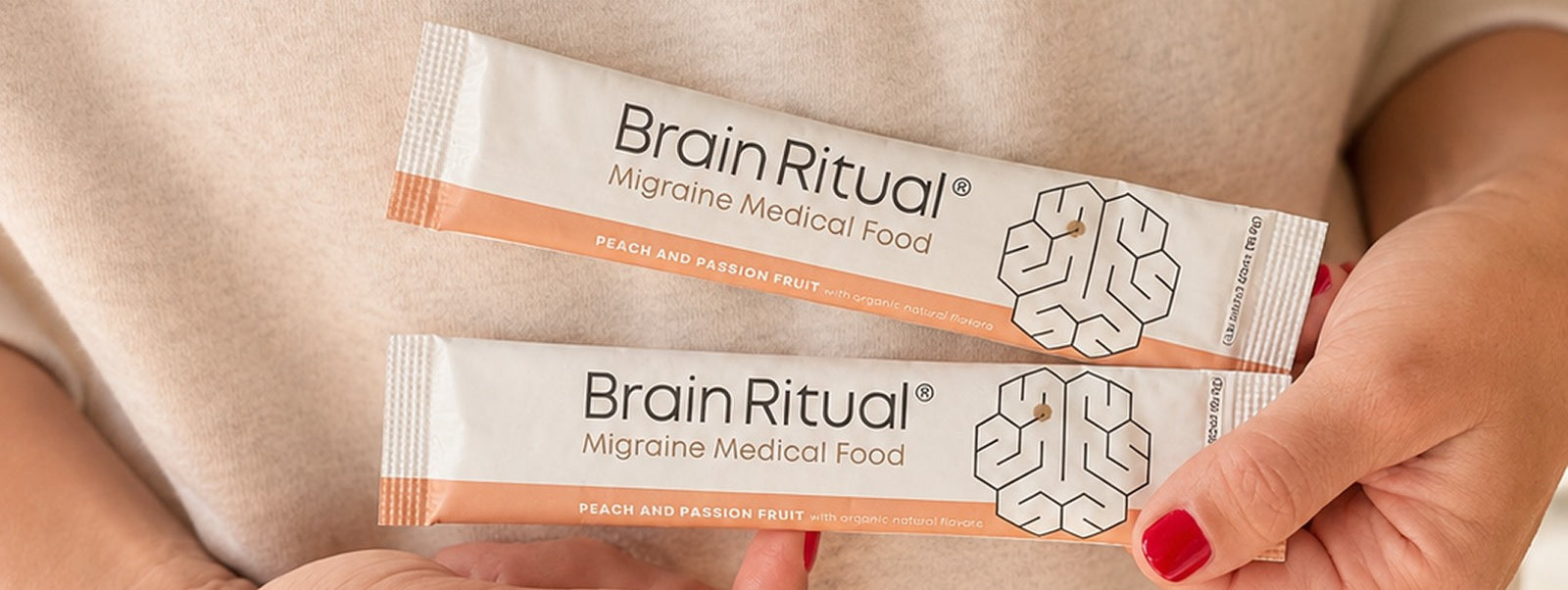 Two Brain Ritual Migraine Medical Food stick packs held against a cream sweater