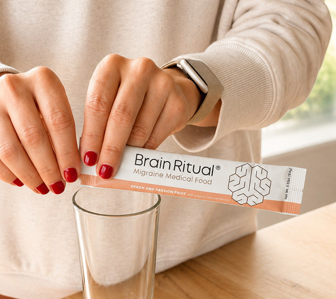 Hands opening a Brain Ritual Migraine Medical Food stick pack above a glass