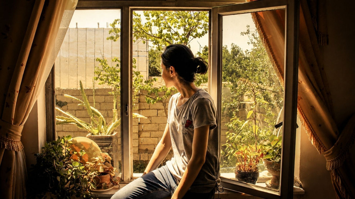 Woman reflecting, looking out a window with soft lighting, for an article on Basilar Migraine vs Vestibular Migraine