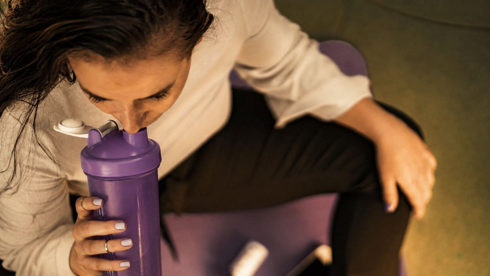 Woman drinking from blender bottle at the gym for an article on creatine and migraines.