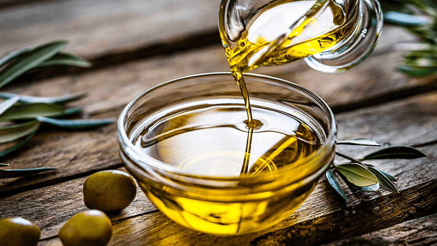 Olive oil being poured into glass bowl with olives on wooden table