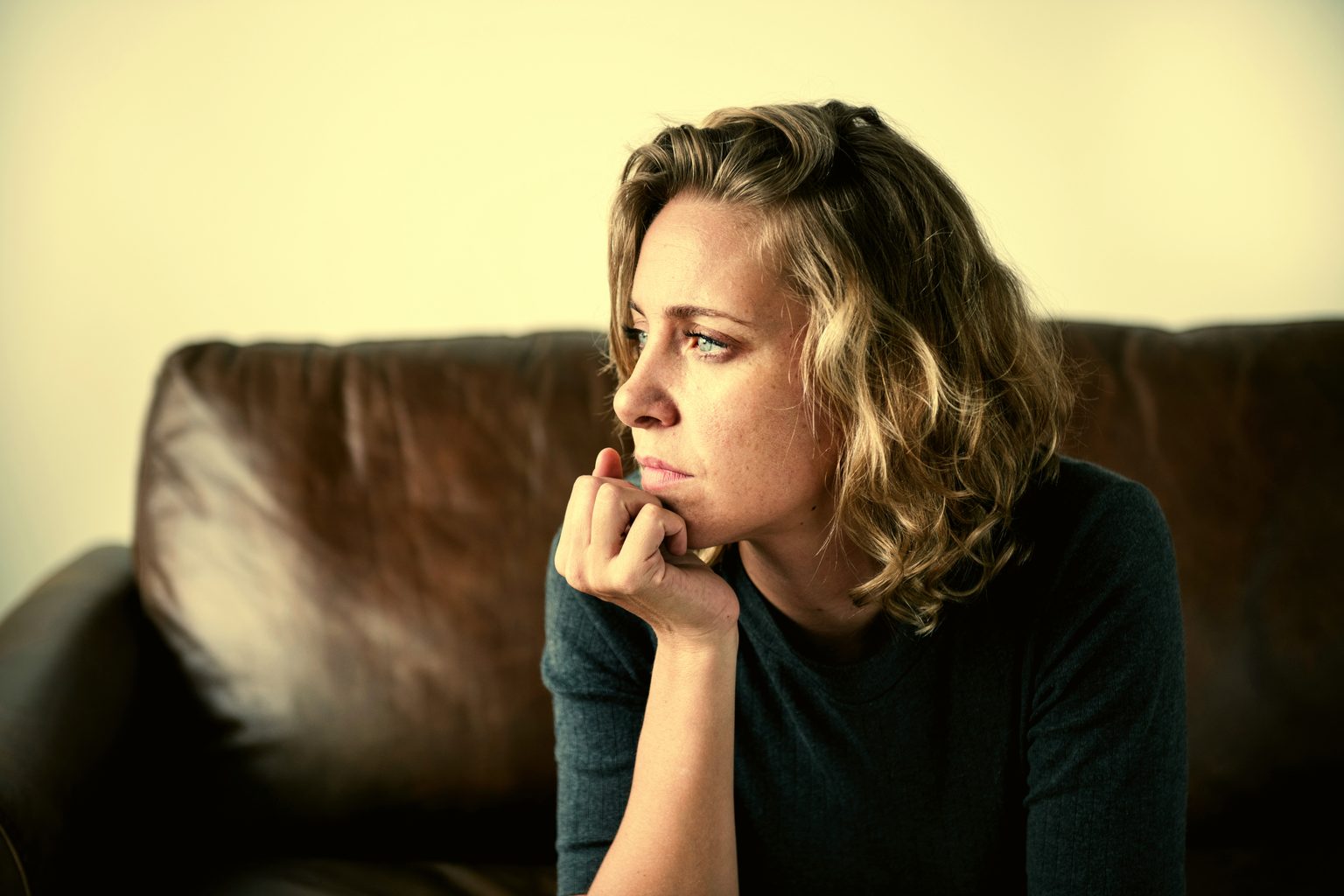 Woman sitting on a sofa in warm light, looking reflective