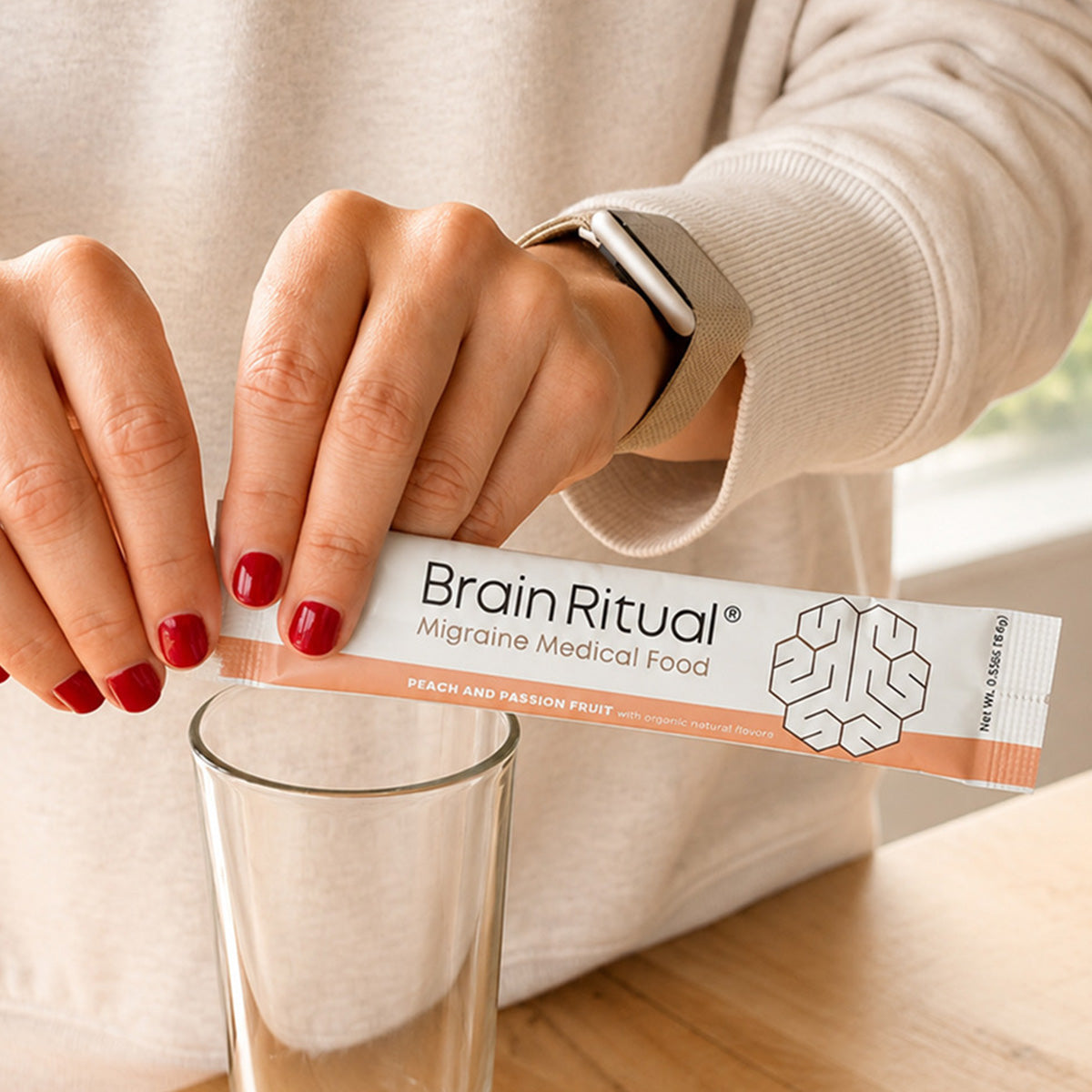Hands tearing open a Brain Ritual stick pack over a glass of water