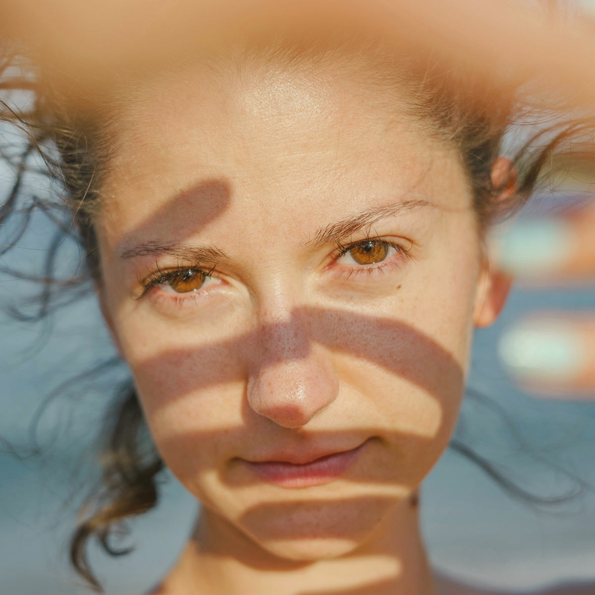 Close-up of a woman outdoors in warm sunlight, dappled shadow across her face