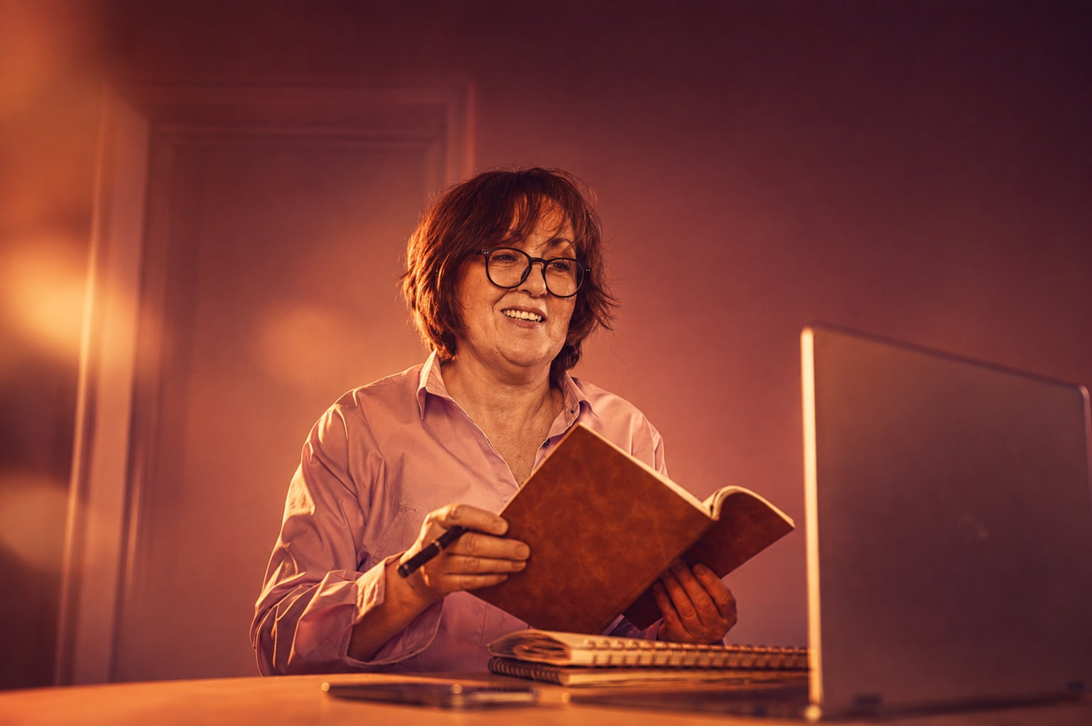Woman holding a notebook beside an open laptop