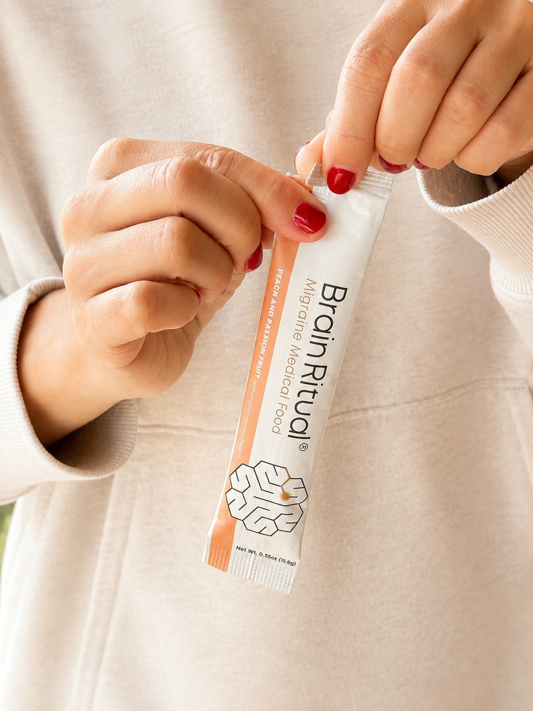 Hands tearing open a Brain Ritual peach and passion fruit stick pack.
