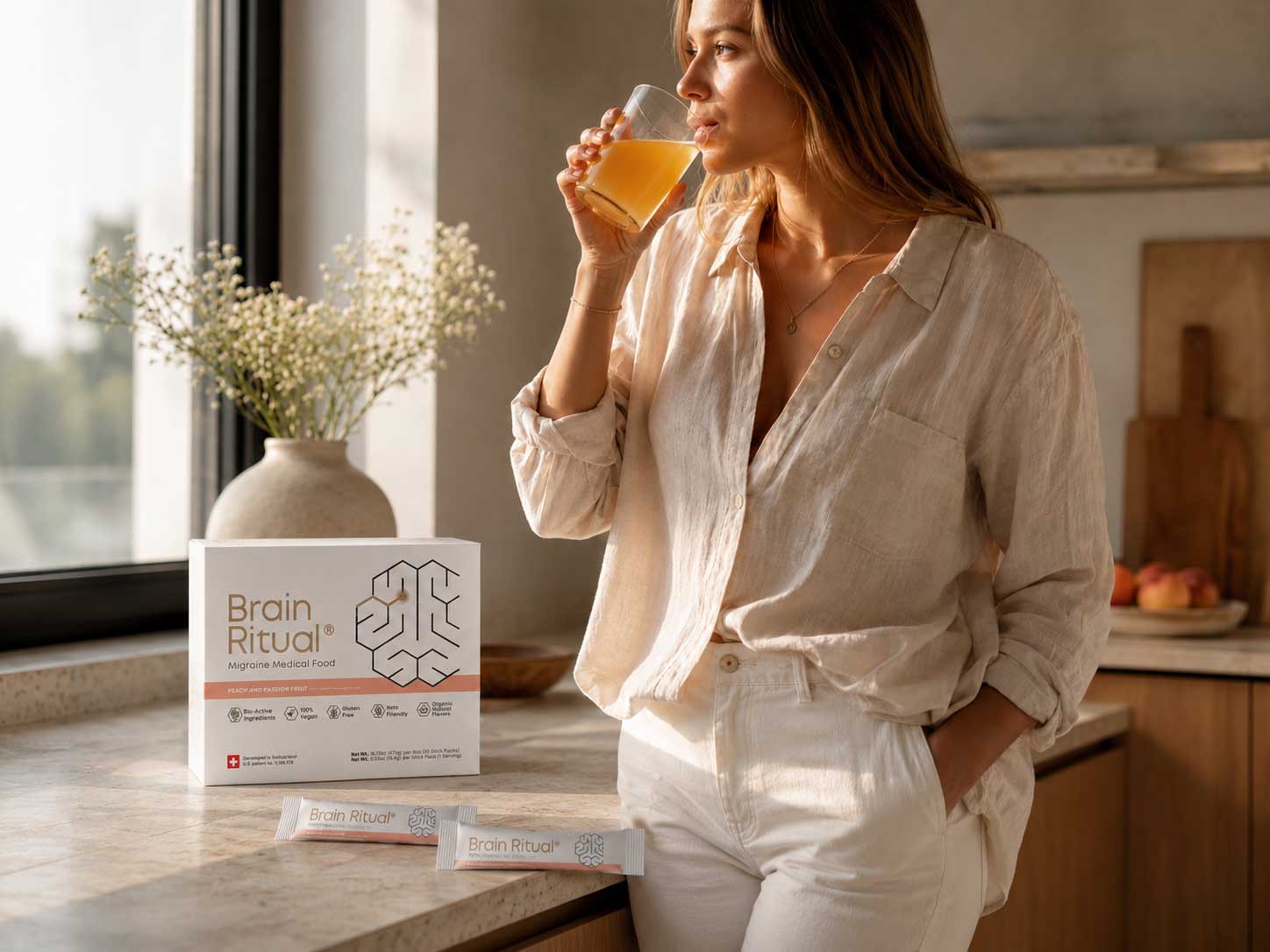 Woman drinking Brain Ritual in a sunlit kitchen with the product box and stick packs on the counter